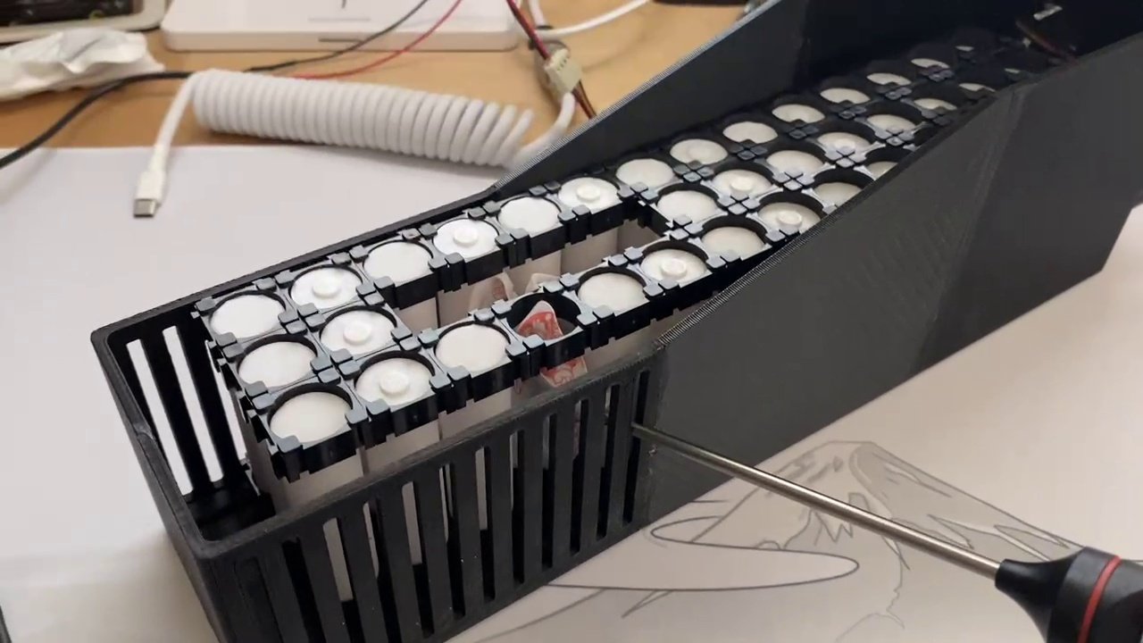 The real pack, lid open — 18650 cells seated in their 3D-printed holder, mid-assembly on the bench.